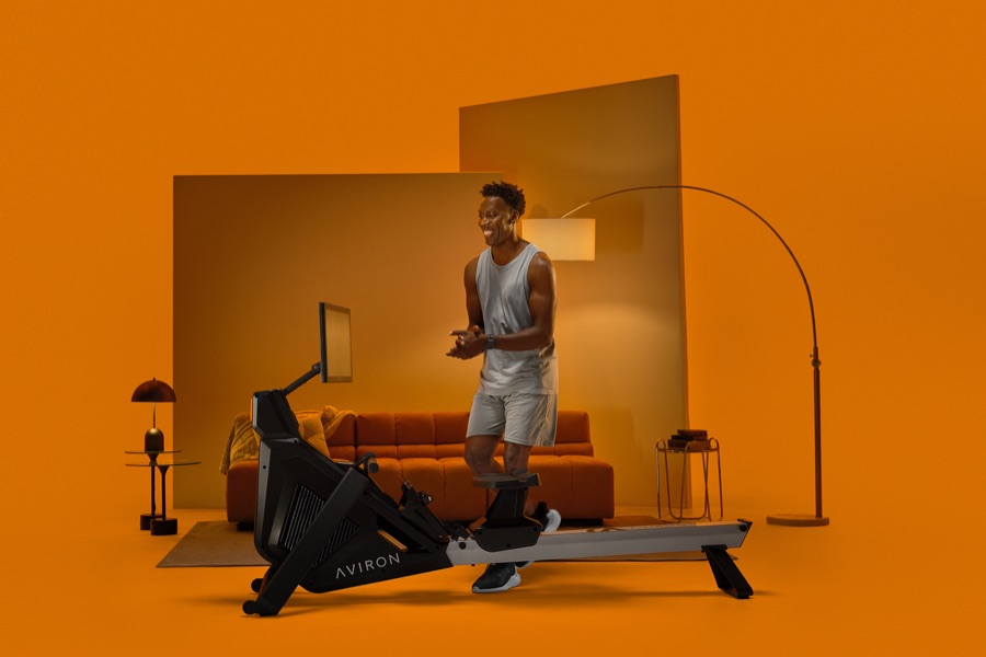 Woman next to the Aviron Strong Rower showing the rotating HD touchscreen in a living room